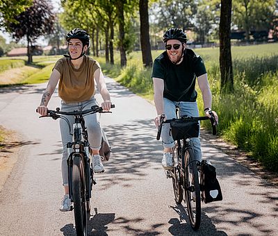Zwei Radfahrer radeln bei Sonnenschein auf der Grenzgängerroute 