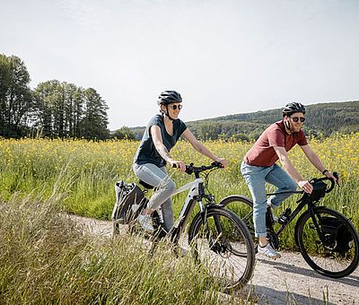 Zwei Radfahrer radeln vor einem Rapsfeld 