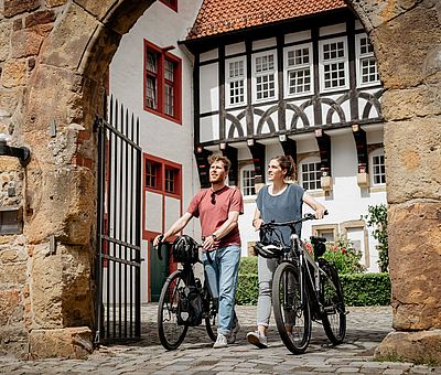 Zwei Radfahrer schieben ihre Fahrräder durch den Innenhof von Schloss Iburg 